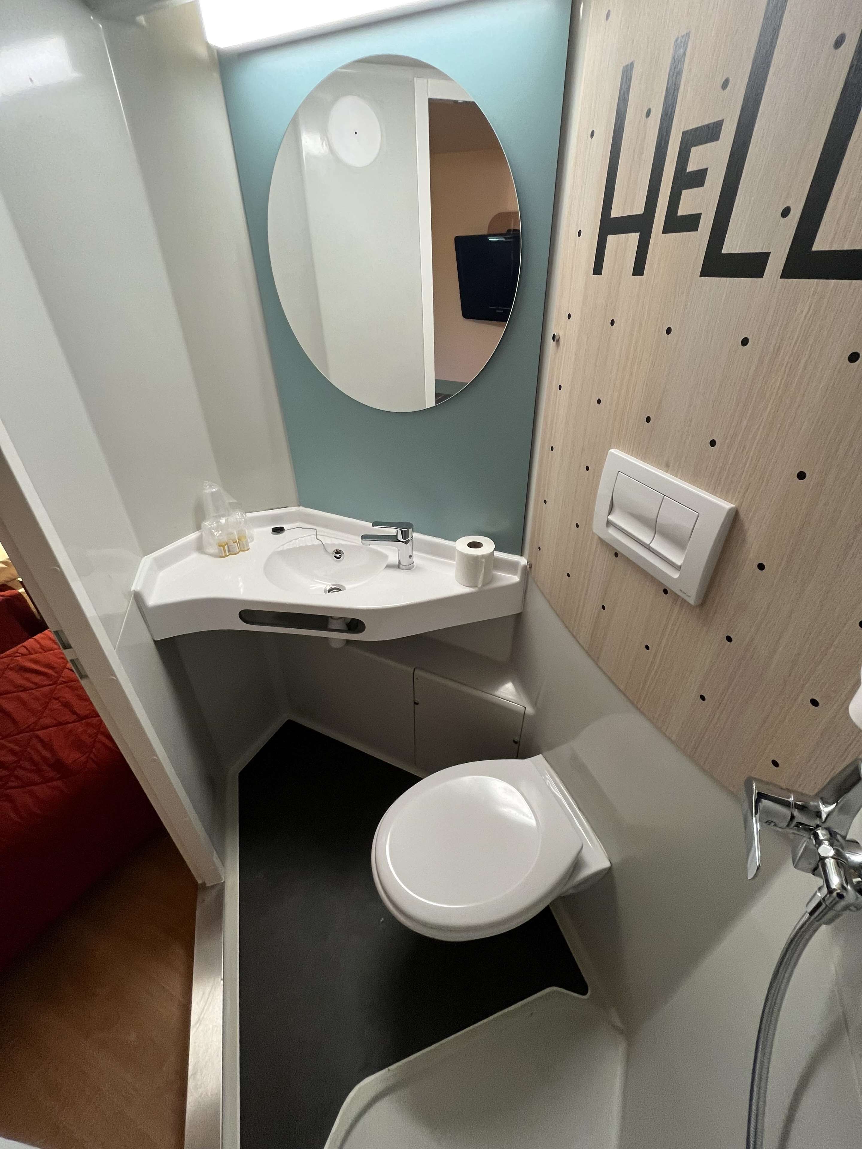 Un baño pequeño con lavamanos blanco, espejo redondo, inodoro y zona de ducha.
