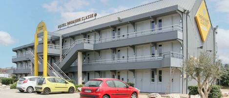 Un hotel con un cartello che riporta la scritta "PREMIERE CLASSE" e una scalinata che conduce all'ingresso. Due automobili sono parcheggiate davanti.