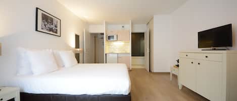 Una habitación de hotel con cama, televisión, escritorio y kitchenette.