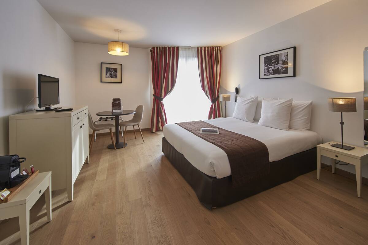 A hotel room with a bed, bedside table, desk, chair, and a television on a dresser.