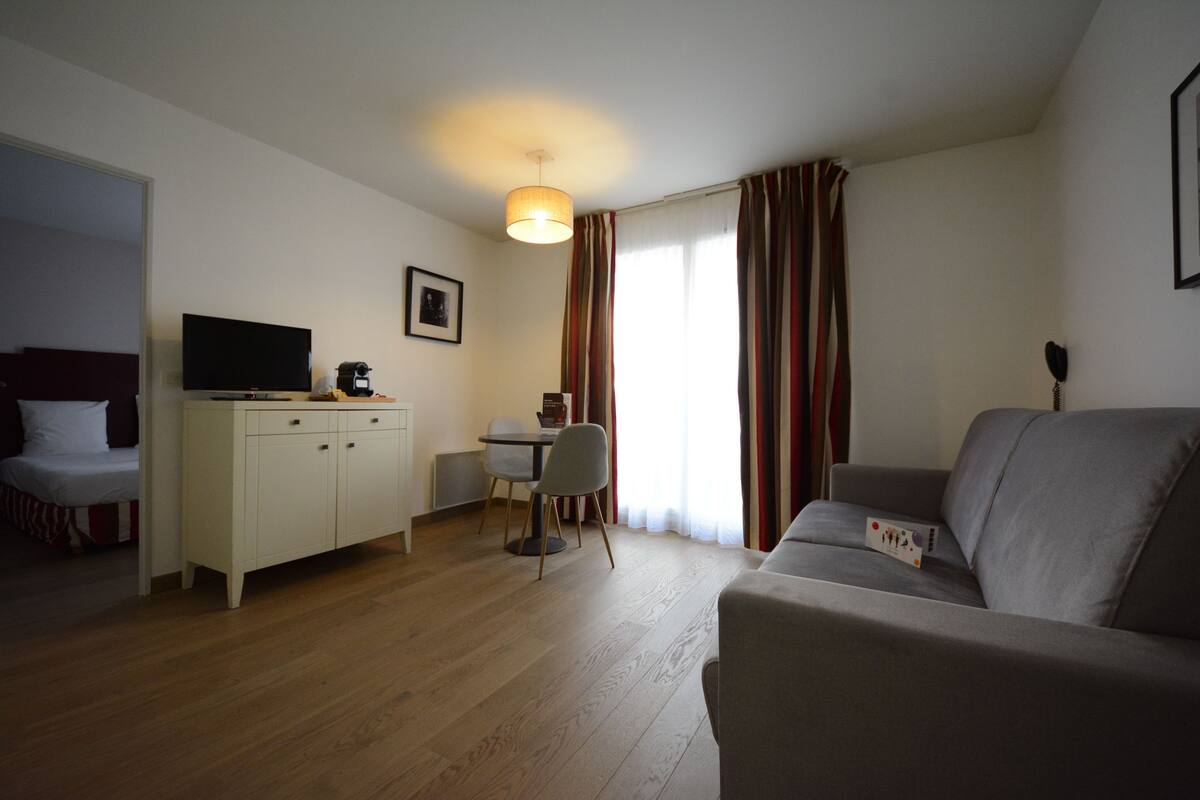 A living room with a sofa, a television, a dining table with chairs, and a kitchen area.