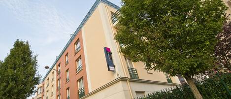 Un edificio de varios pisos con fachada color beige, balcones verdes y un letrero que indica que es una residencia.