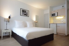 Une chambre à coucher comprenant un lit, des tables de chevet, une commode, une lampe fixée au mur, un tableau encadré, un four à micro-ondes et un petit réfrigérateur.