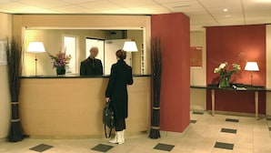 Un espace d’accueil avec un comptoir de réception en bois, un miroir et deux lampes. Des plantes décoratives sont disposées de part et d’autre du comptoir.