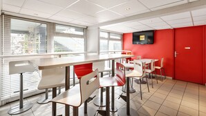 A modern cafeteria with white and red tables and chairs, large windows, and a red wall with a television.