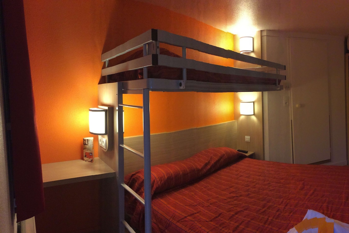 Un lit superposé avec une couvre-lit rouge, une table de chevet avec une lampe et un radiateur fixé au mur.
