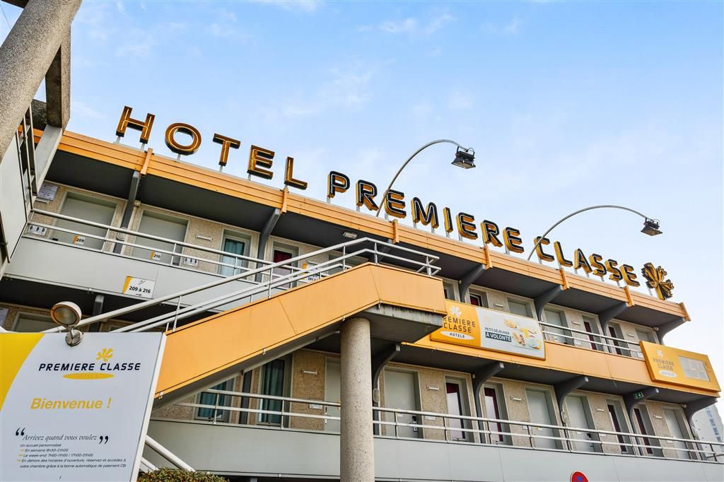 Un hôtel avec une enseigne indiquant « HÔTEL PREMIÈRE CLASSE » et une pancarte de bienvenue en dessous.