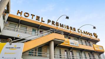 Un hôtel avec une enseigne indiquant « HÔTEL PREMIÈRE CLASSE » et une pancarte de bienvenue en dessous.