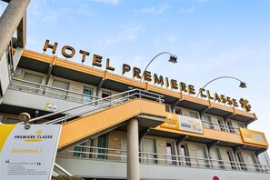 Un hôtel avec une enseigne indiquant « HÔTEL PREMIÈRE CLASSE » et une pancarte de bienvenue en dessous.