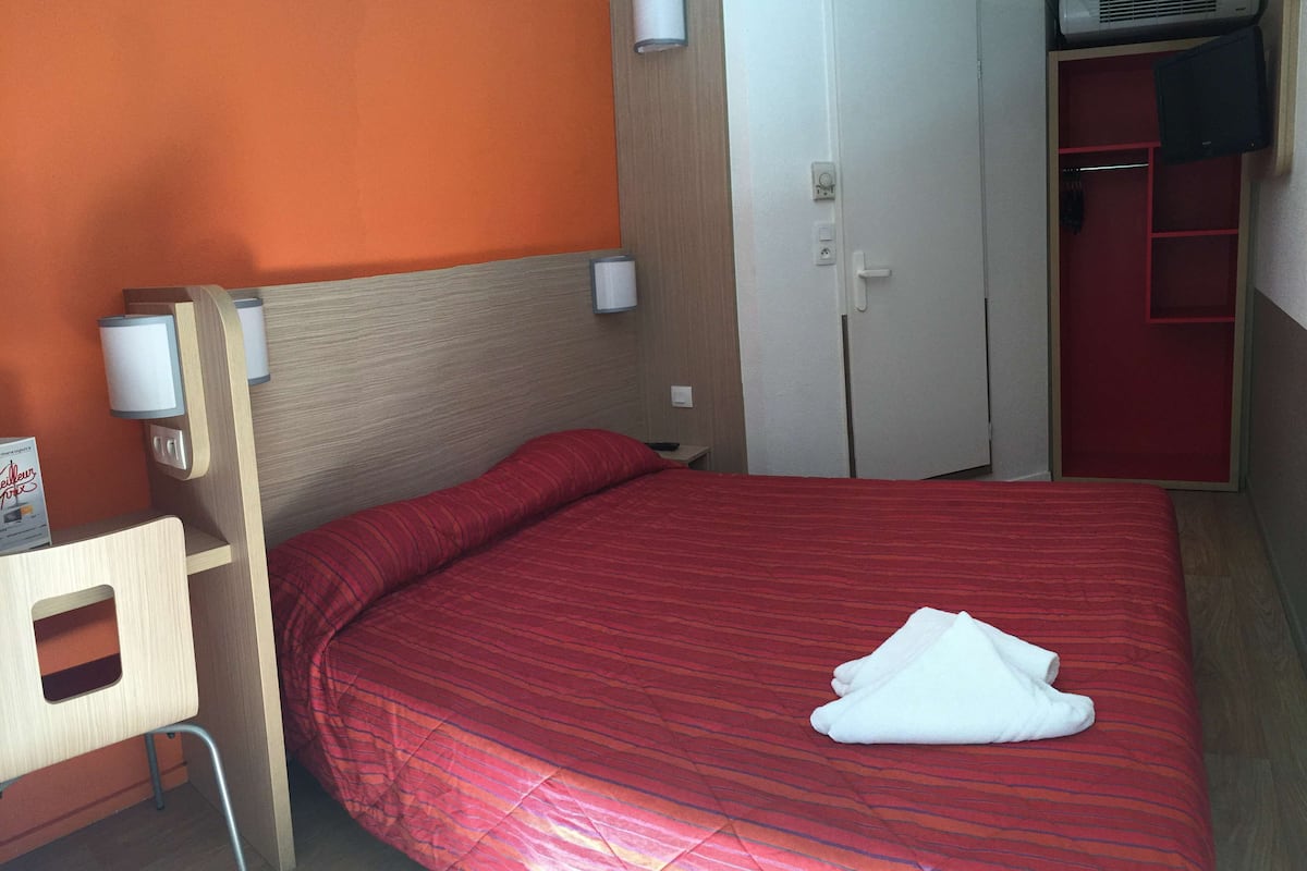 Una habitación de hotel con una cama, un escritorio de madera, un armario y un televisor.