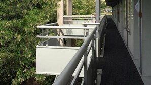 A corridor with a railing, a concrete structure with an arch, and greenery in the background.