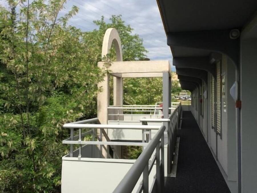 A corridor with a railing, a concrete structure with an arch, and greenery in the background.