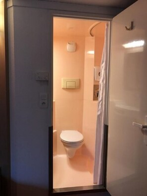 Ein kleines Badezimmer mit Toilette, Duschvorhang und Lichtschalter an der Wand.