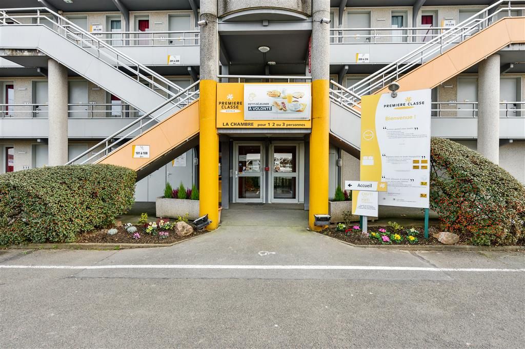 L’entrée d’un hôtel, avec un escalier, une enseigne indiquant « Première Classe » et un panneau d’accueil.