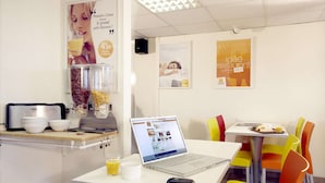 A modern cafe with a laptop on a table, a coffee machine, and colorful chairs. - Hotel Première Classe Salon De Provence (Salon-de-Provence)