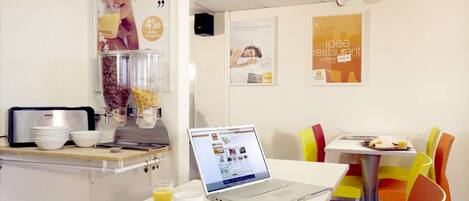 A modern cafe with a laptop on a table, a coffee machine, and colorful chairs.