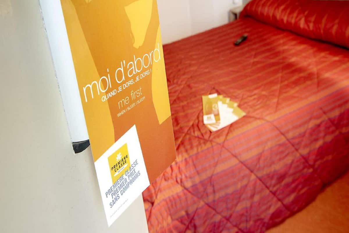 Una habitación de hotel con una cama, un almohadón y un cartel en la pared.
