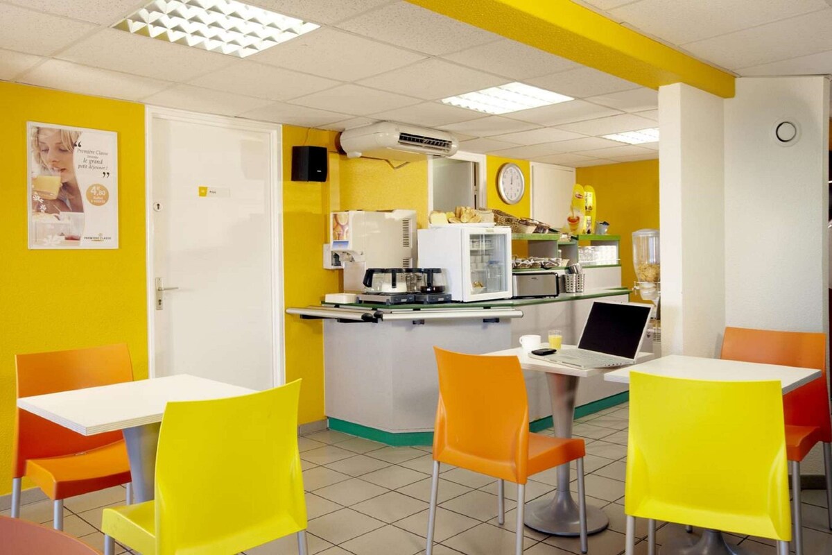 A brightly colored cafe with yellow and orange chairs, a white counter, and a laptop on the table.