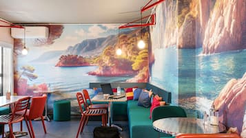 A room with a mural of a coastal landscape, a round table with chairs, a sofa, and a laptop on the sofa.