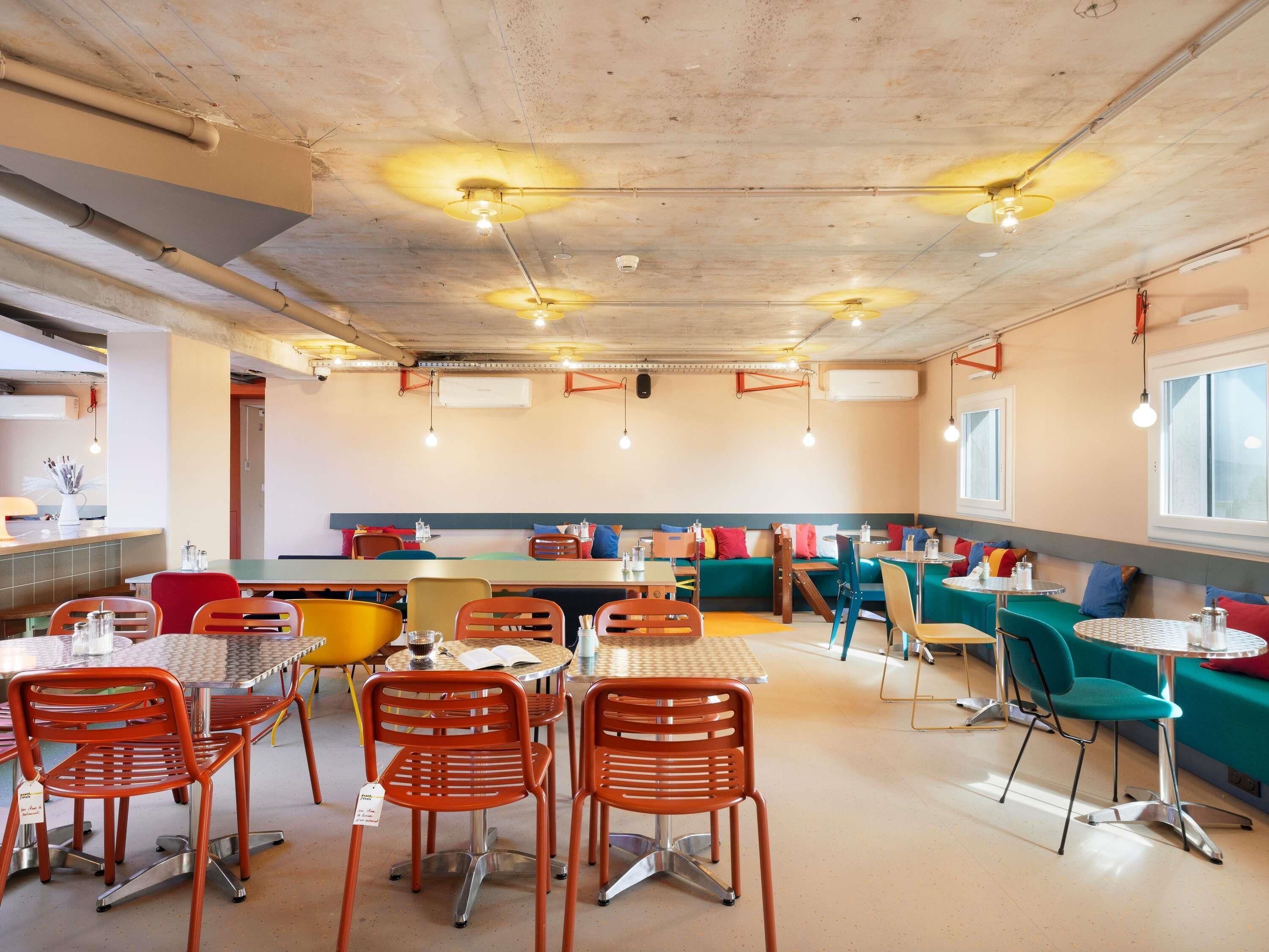 A restaurant with round tables and orange chairs, a counter with a cash register, and a seating area with teal cushions.