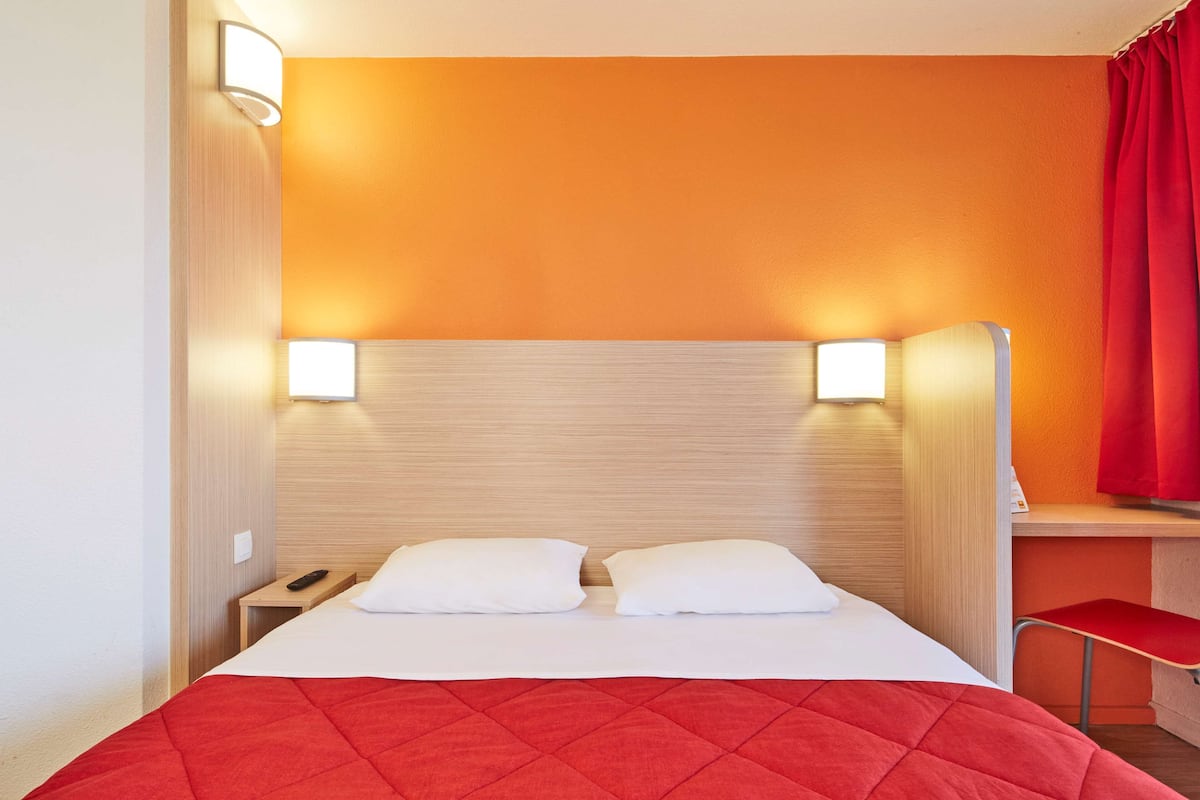 A hotel room with a bed, two bedside lamps, a desk, and a chair.