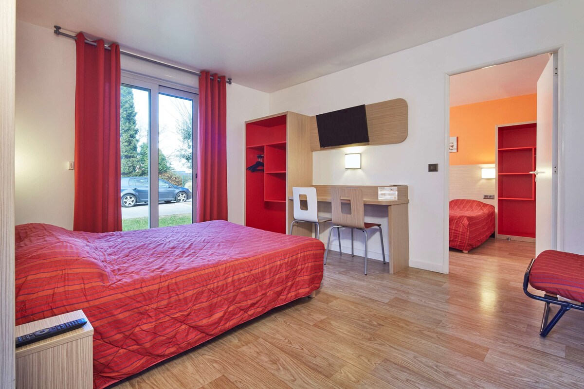 A hotel room with a large bed, a desk, a chair, and a small seating area.