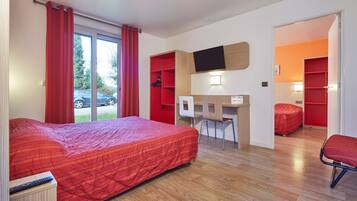 A hotel room with a large bed, a desk, a chair, and a small seating area.