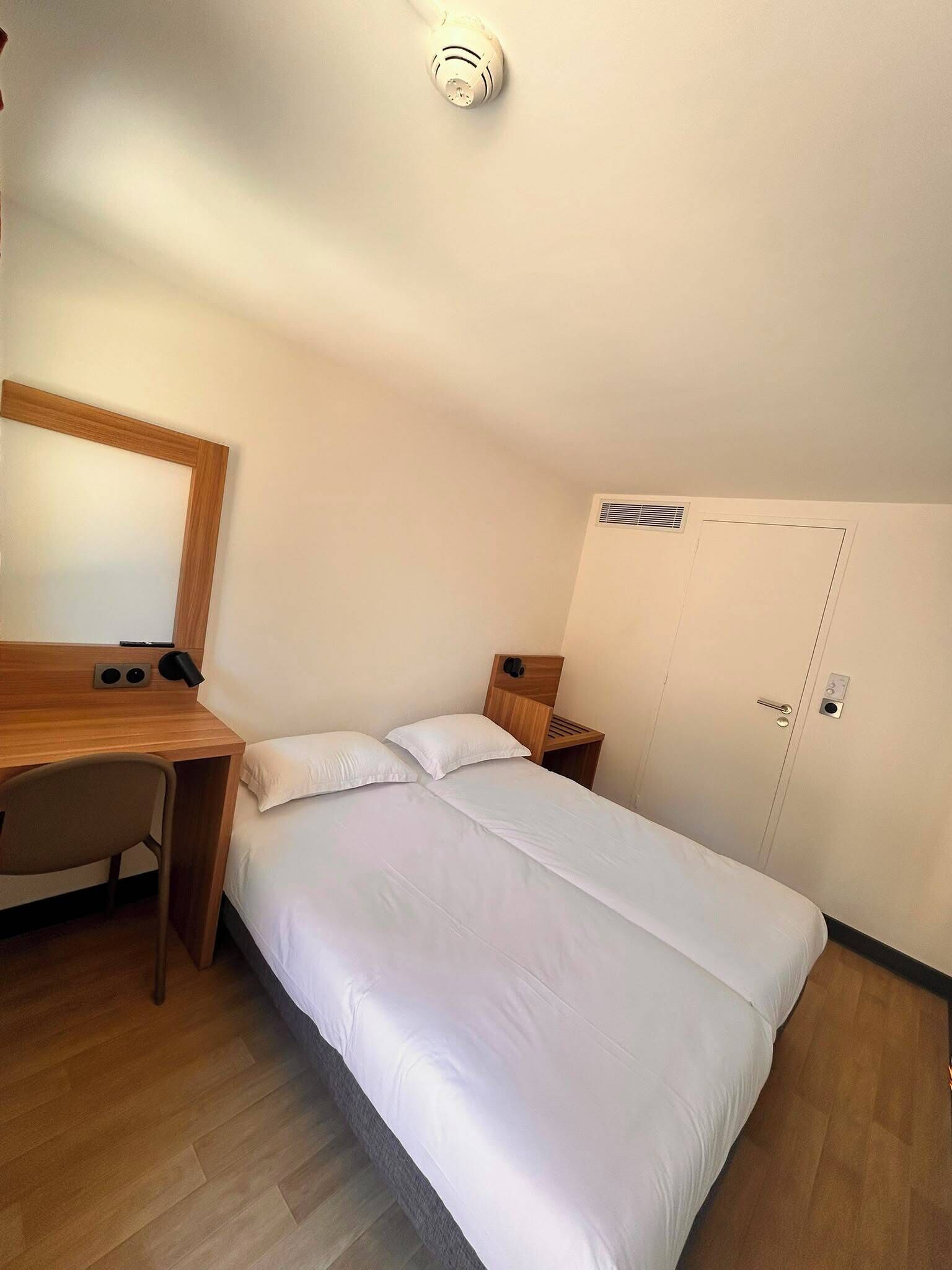 Une pièce comprenant un lit, un bureau, une chaise, un miroir, une armoire et un luminaire au plafond.