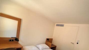Une pièce comprenant un lit, un bureau, une chaise, un miroir, une armoire et un luminaire au plafond.