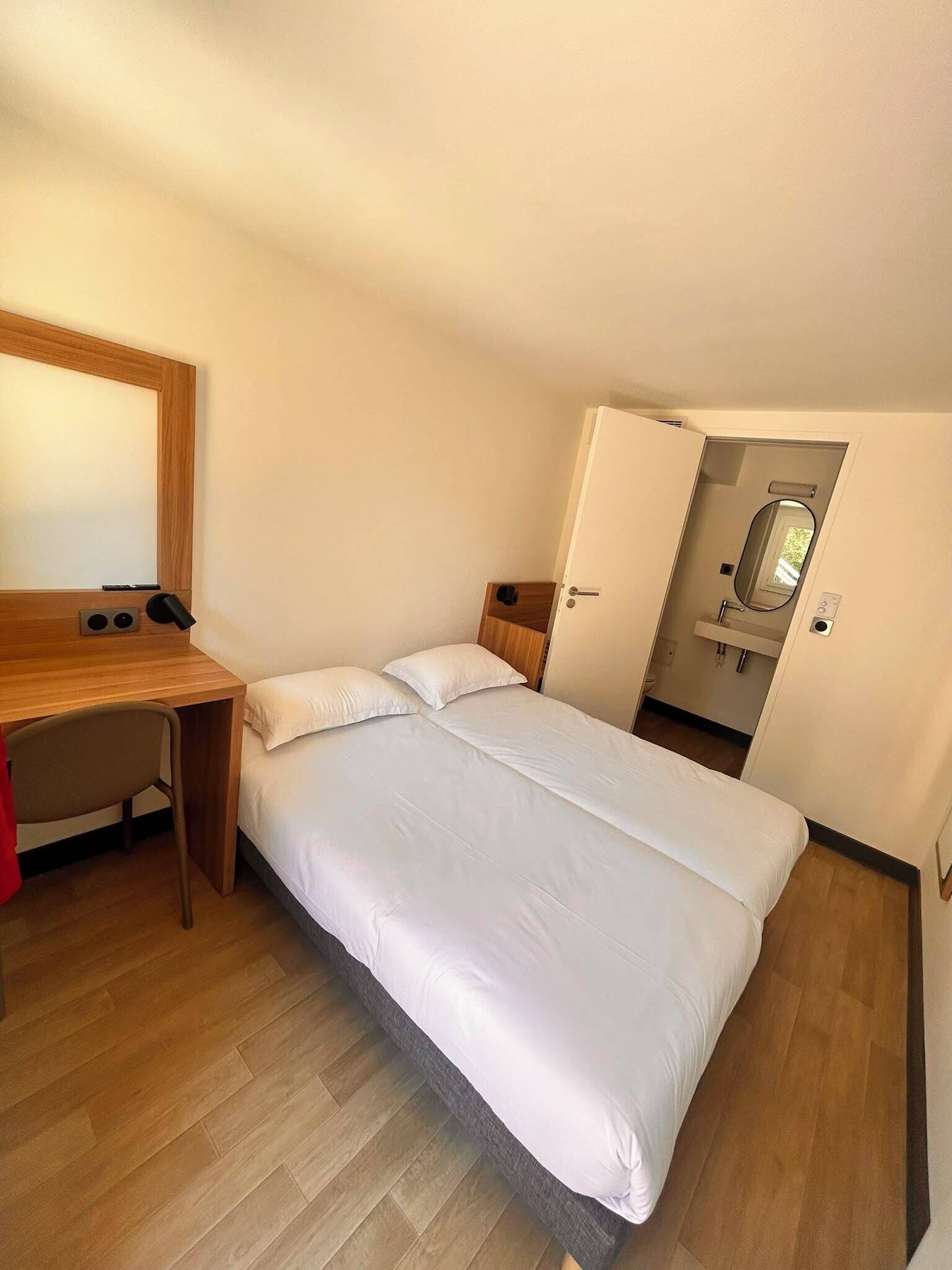 A bedroom with a bed, a desk, and a mirror.