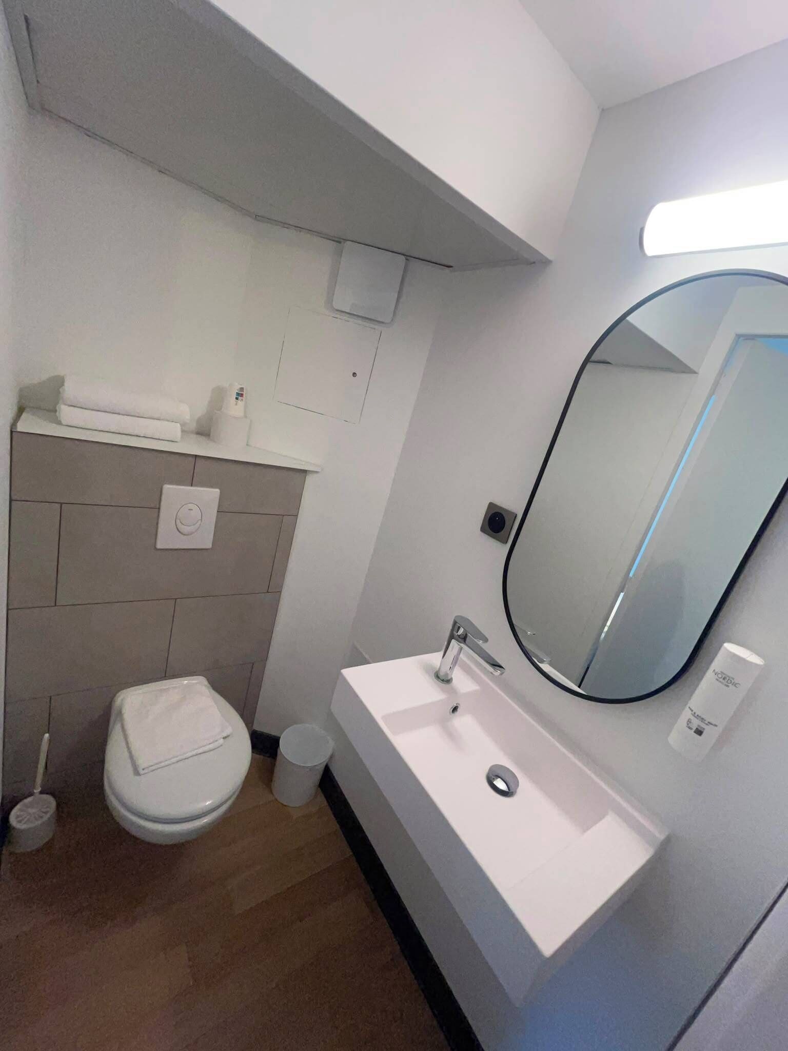 A modern bathroom with a white sink, a mirror, a toilet, and a towel rack.