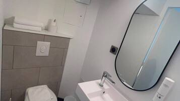 A modern bathroom with a white sink, a mirror, a toilet, and a towel rack.