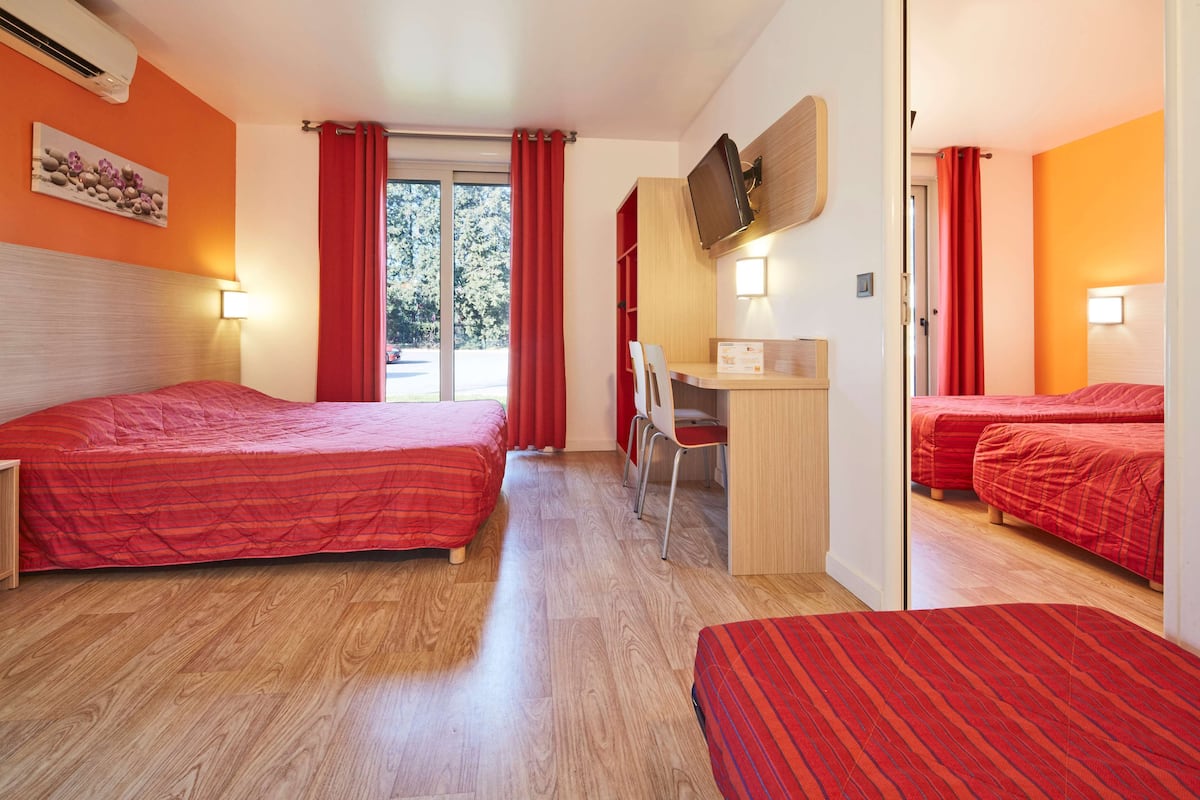 A hotel room with two beds, a desk, a chair, and a TV on the wall.