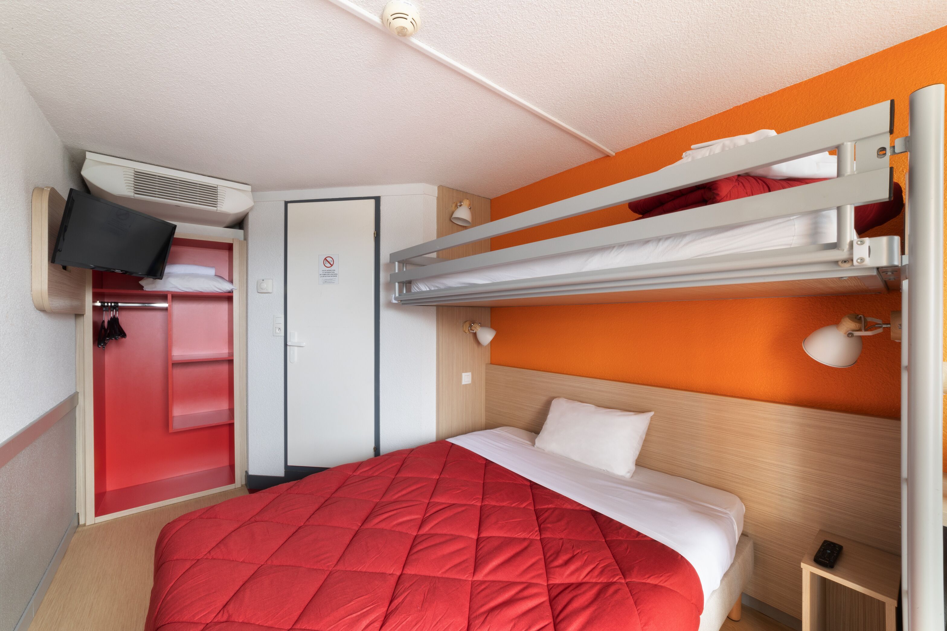 Una habitación de hotel con literas, televisión, armario y escritorio.