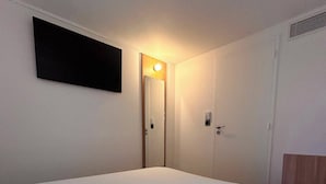 Un dormitorio con cama, una puerta y una lámpara fijada a la pared.