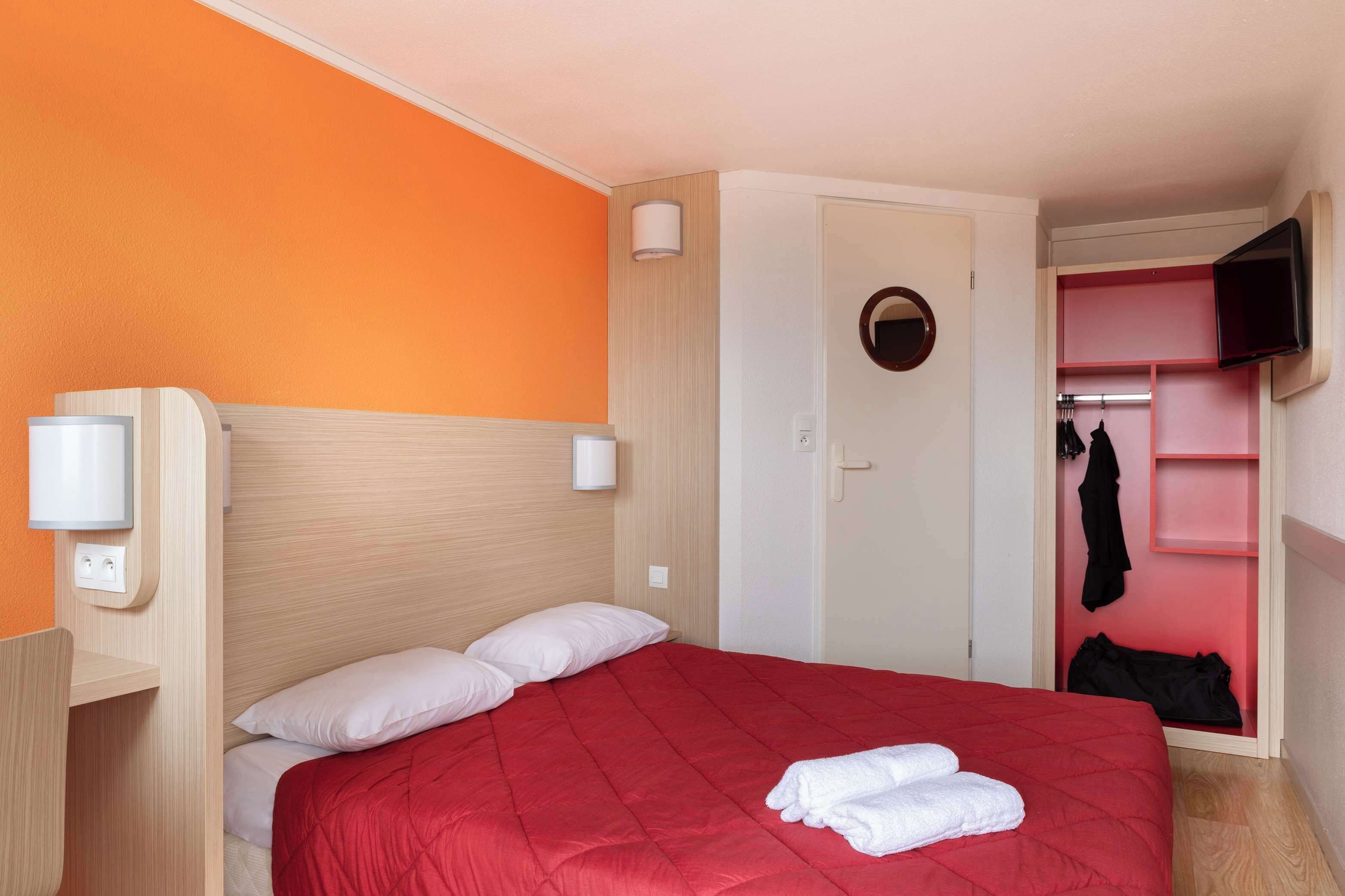 A hotel room with a bed, a TV, a wardrobe, and a mirror.