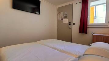 Una habitación con dos camas, un televisor de pantalla plana montado en la pared, una puerta con cerradura y una ventana con cortina roja.