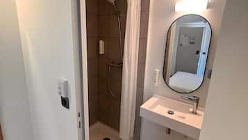 Une salle de bain moderne avec une douche à l’italienne, un lavabo avec un miroir et un luminaire placé au-dessus du miroir.