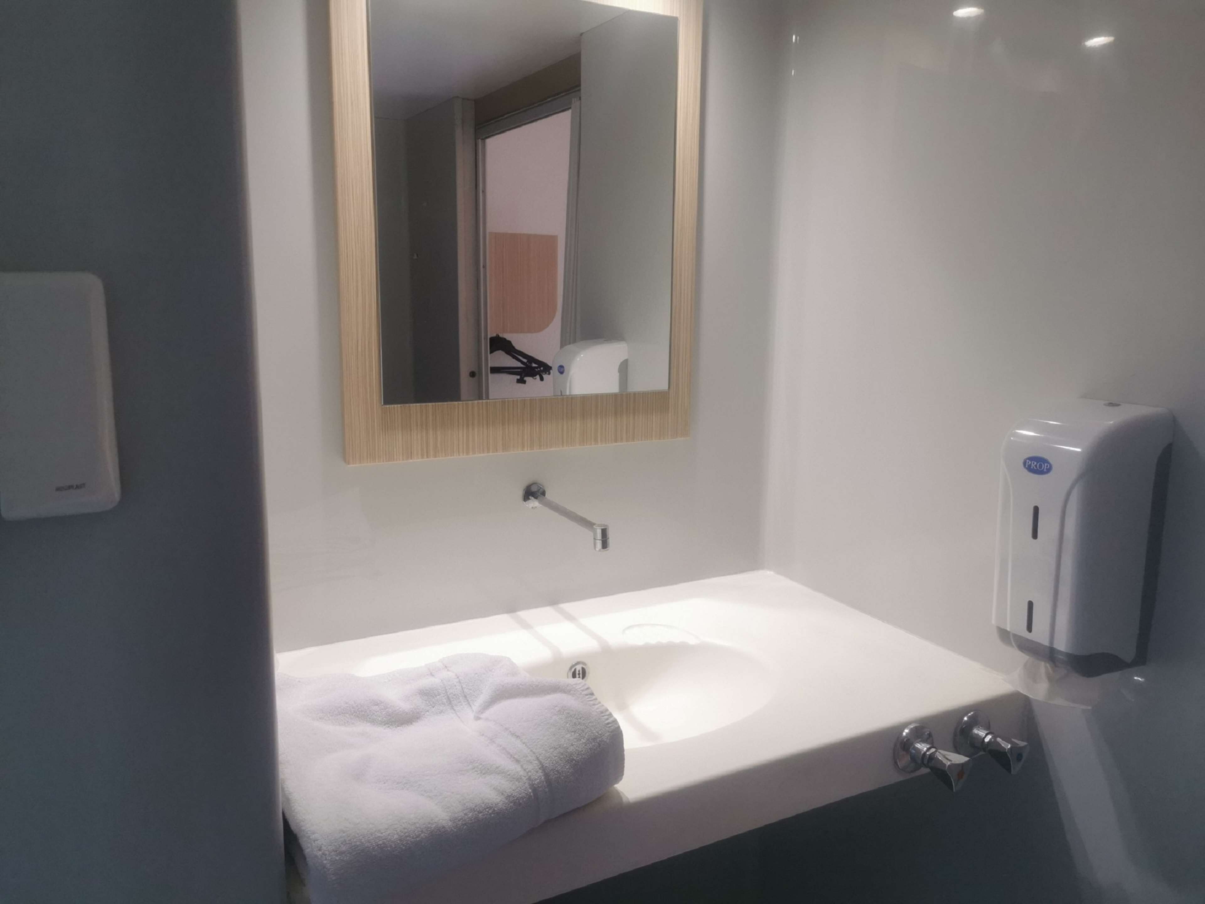 A modern bathroom with a white sink, a mirror, and a hand sanitizer dispenser.