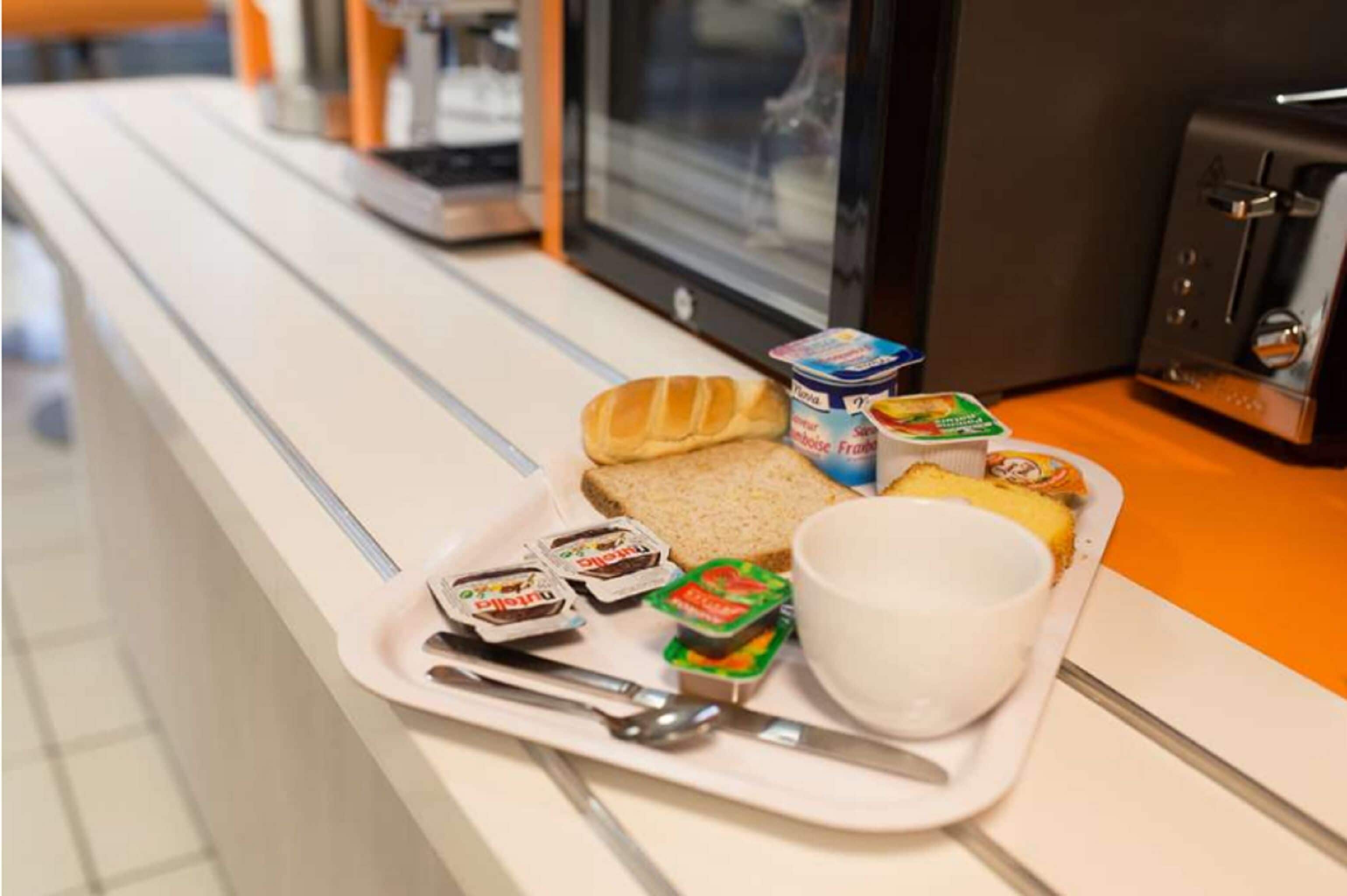 Una bandeja con un sándwich, yogur y una taza sobre una encimera.