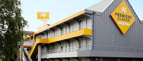 Un hotel con una fachada destacada en amarillo y gris, una escalera que conduce a la entrada y un cartel que indica que es un hotel 'Premiere Classe'.
