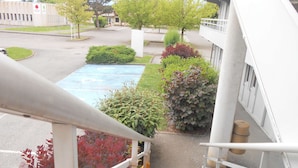 A parking lot with a blue parking space, a staircase leading to a building, and various trees and shrubs. - Hôtel Premiere Classe Grenoble Sud - Gières Université (Gieres)