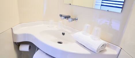A white bathroom sink with a mirror above it, a towel rack, and a toilet paper holder.