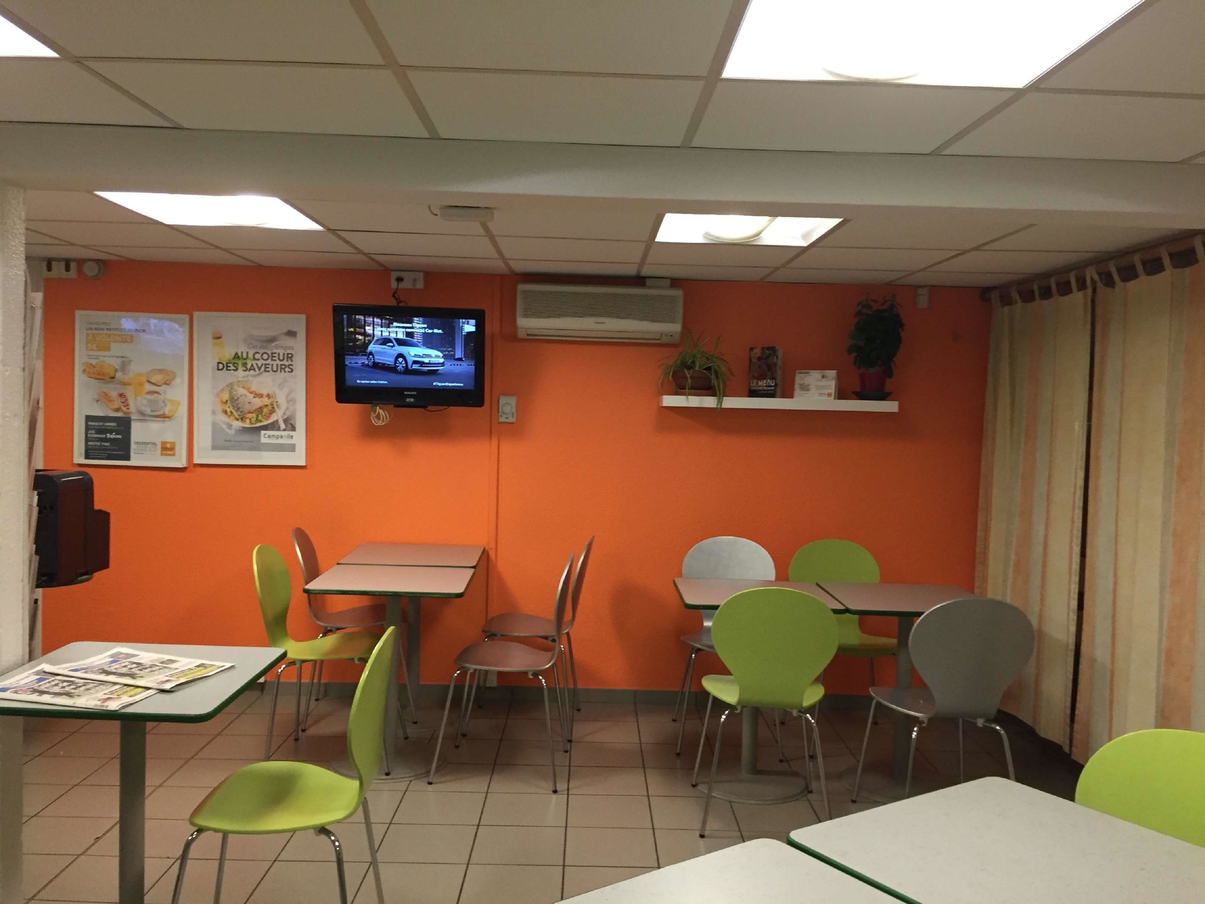 A restaurant with orange walls, a TV on the wall, and several tables and chairs.