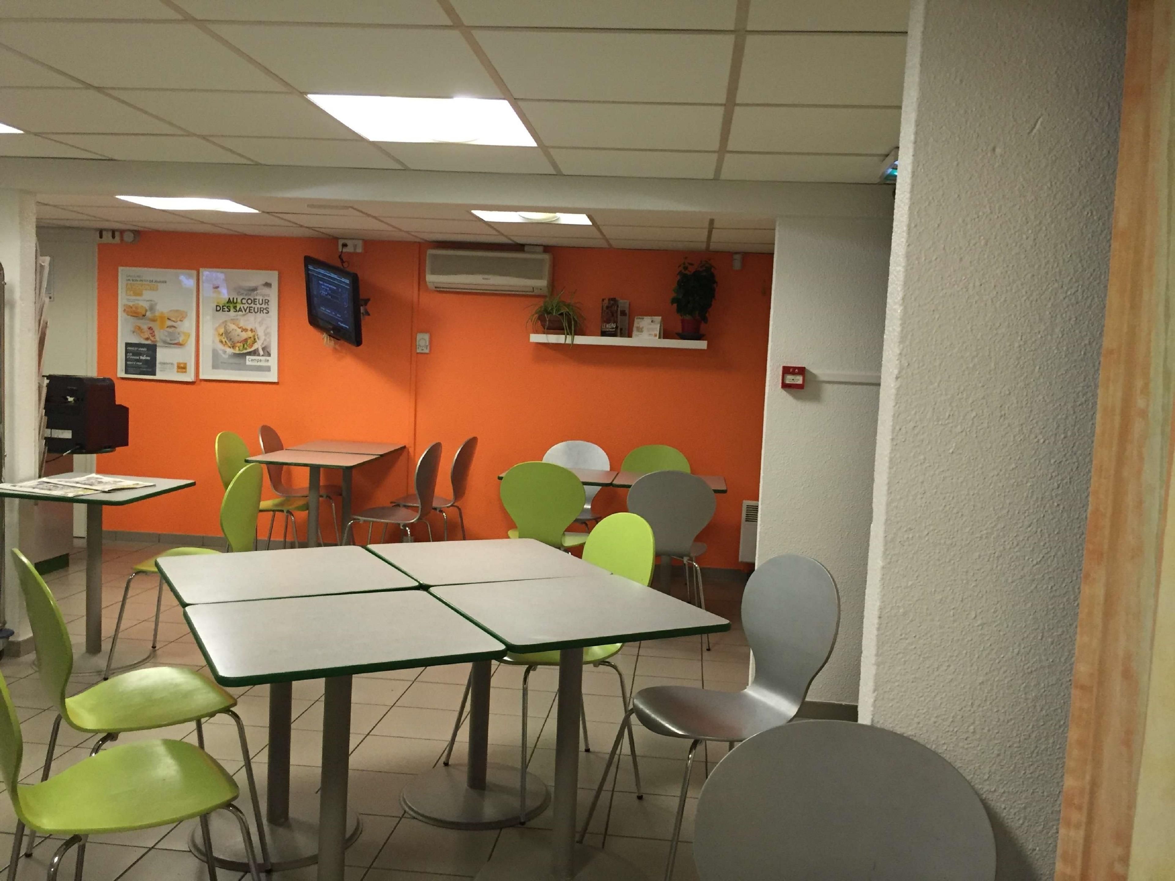 A dining area with tables and chairs, an air conditioning unit, and a television on the wall.