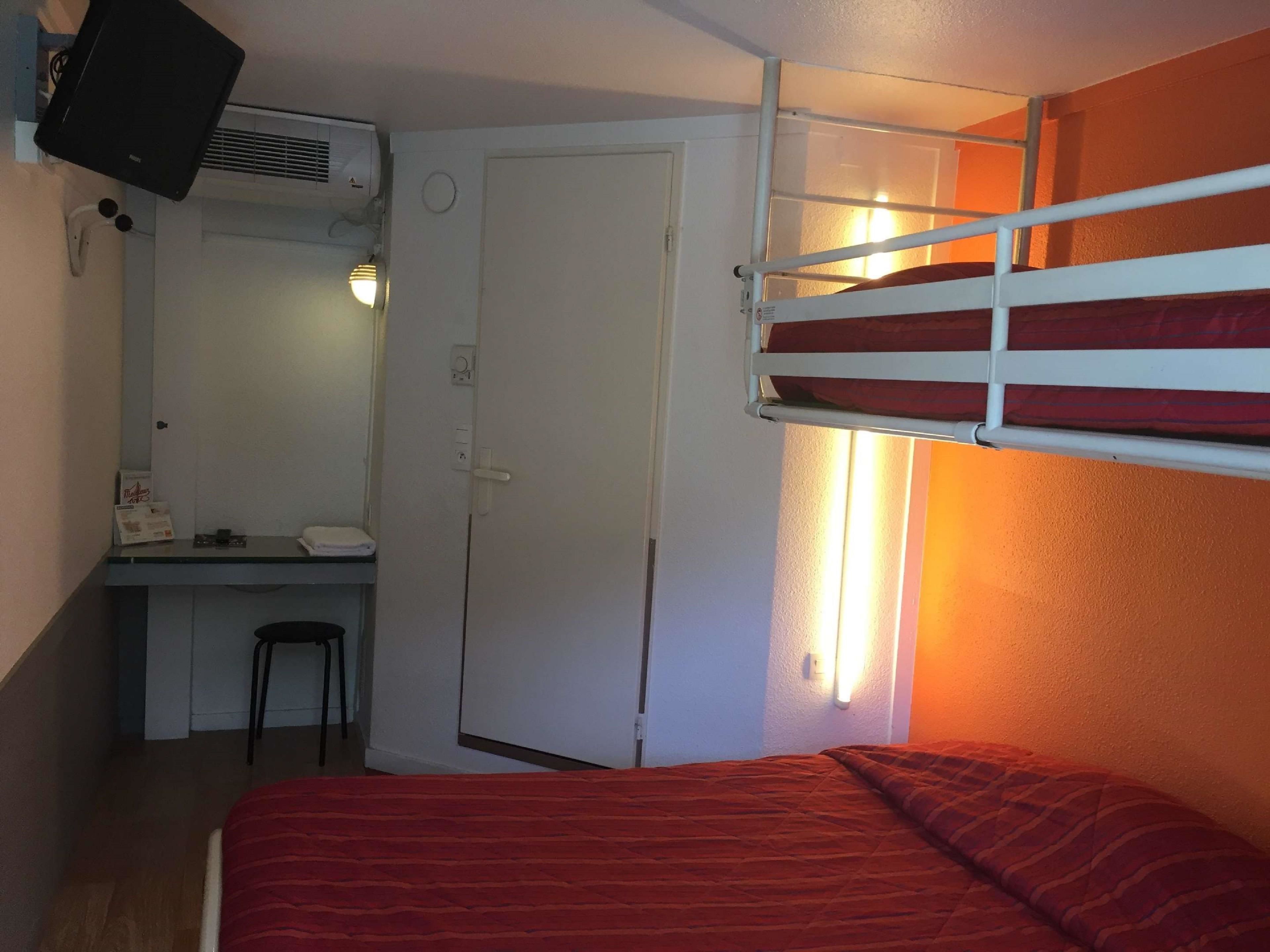 Una stanza piccola con un letto a castello, una scrivania con una sedia, uno specchio e una porta.