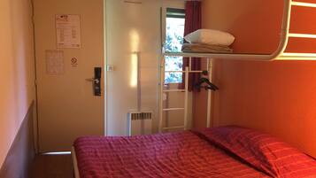 A bunk bed room with a red bedspread, a door with a notice, a window with curtains, and a coat rack.