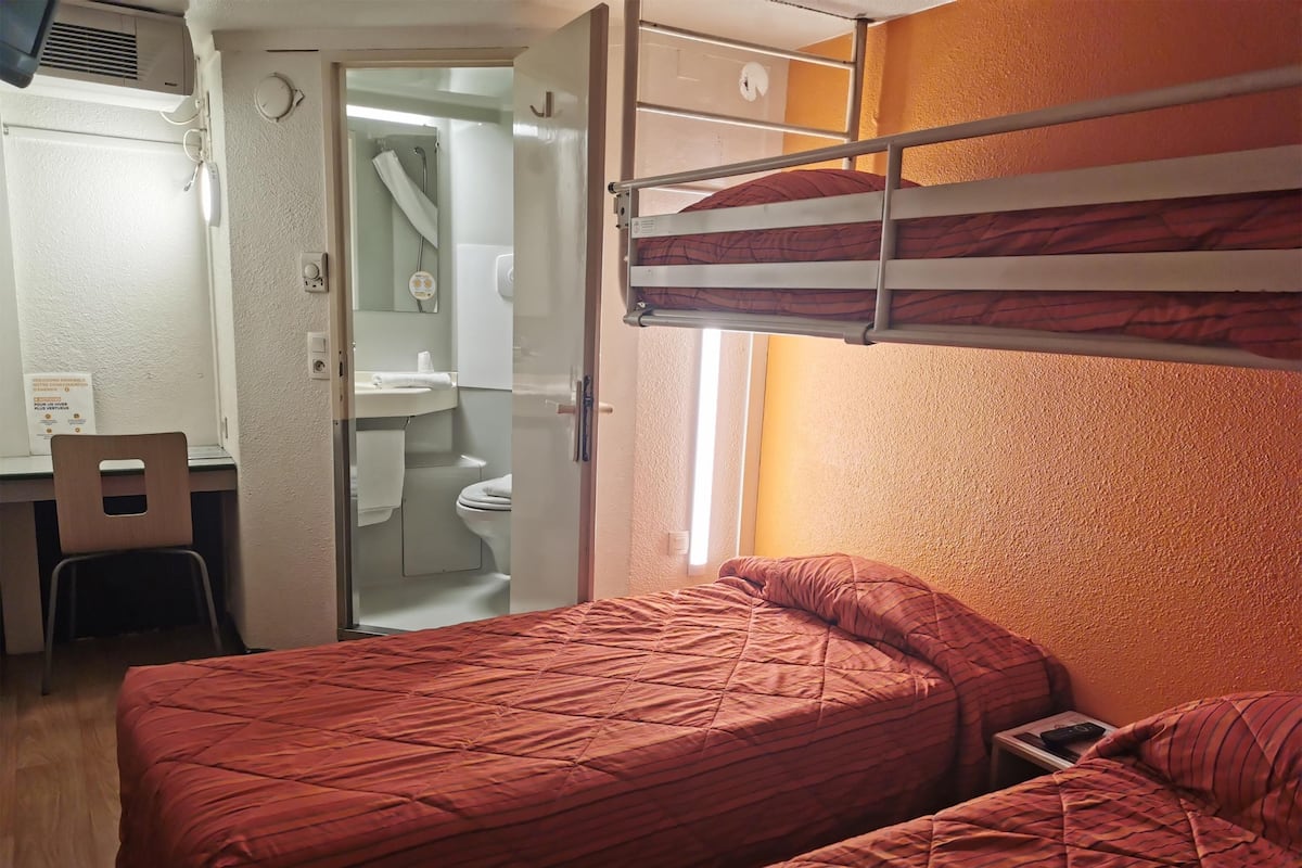 Habitación tipo dormitorio con camas literas, un escritorio y un baño visible a través de una puerta abierta.