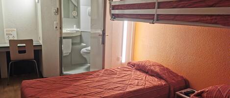 A dormitory room with bunk beds, a desk, and a bathroom visible through an open door.
