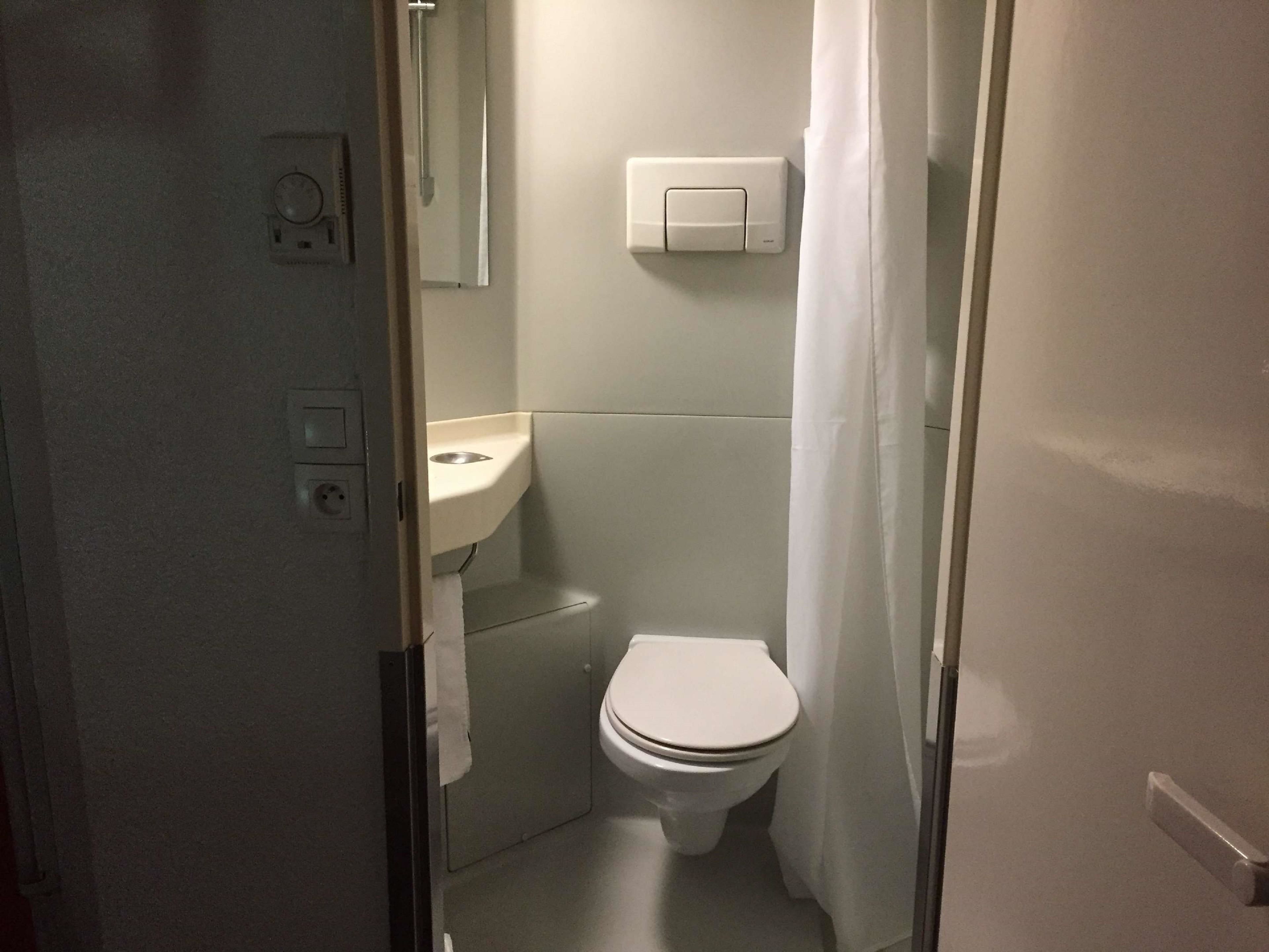 A small, narrow bathroom with a toilet, sink, and a towel hanging on the wall.